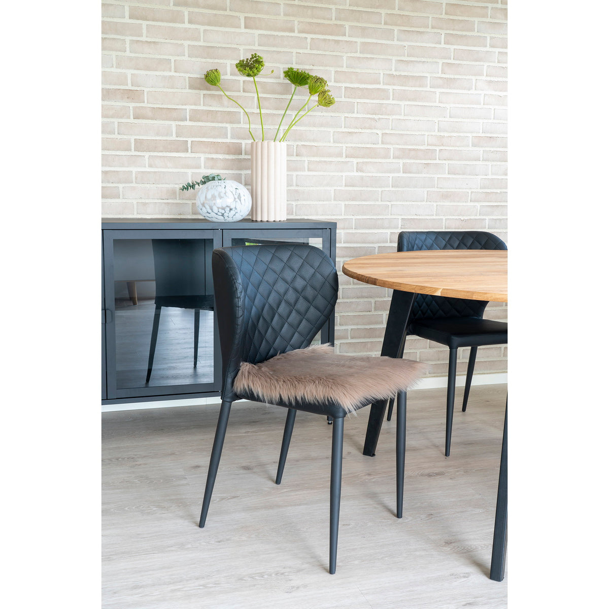 Galette en fausse fourrure mushroom posée sur une chaise noire matelassée près d'une table ronde en bois