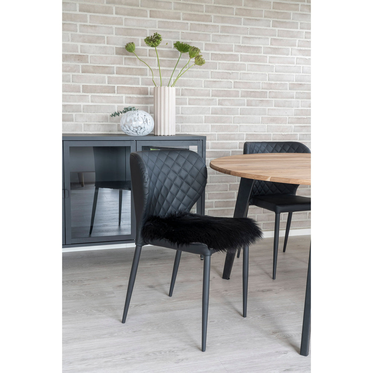 Galette en fausse fourrure noire posée sur une chaise noire matelassée près d'une table ronde en bois