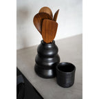 Gobelet en terre cuite noire sur un plan de travail à côté d'un pot à ustensiles noir garni de spatules en bois