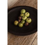 Coupe Bowlzilla en bois noirci garnie de pommes vertes sur une table en bois brut