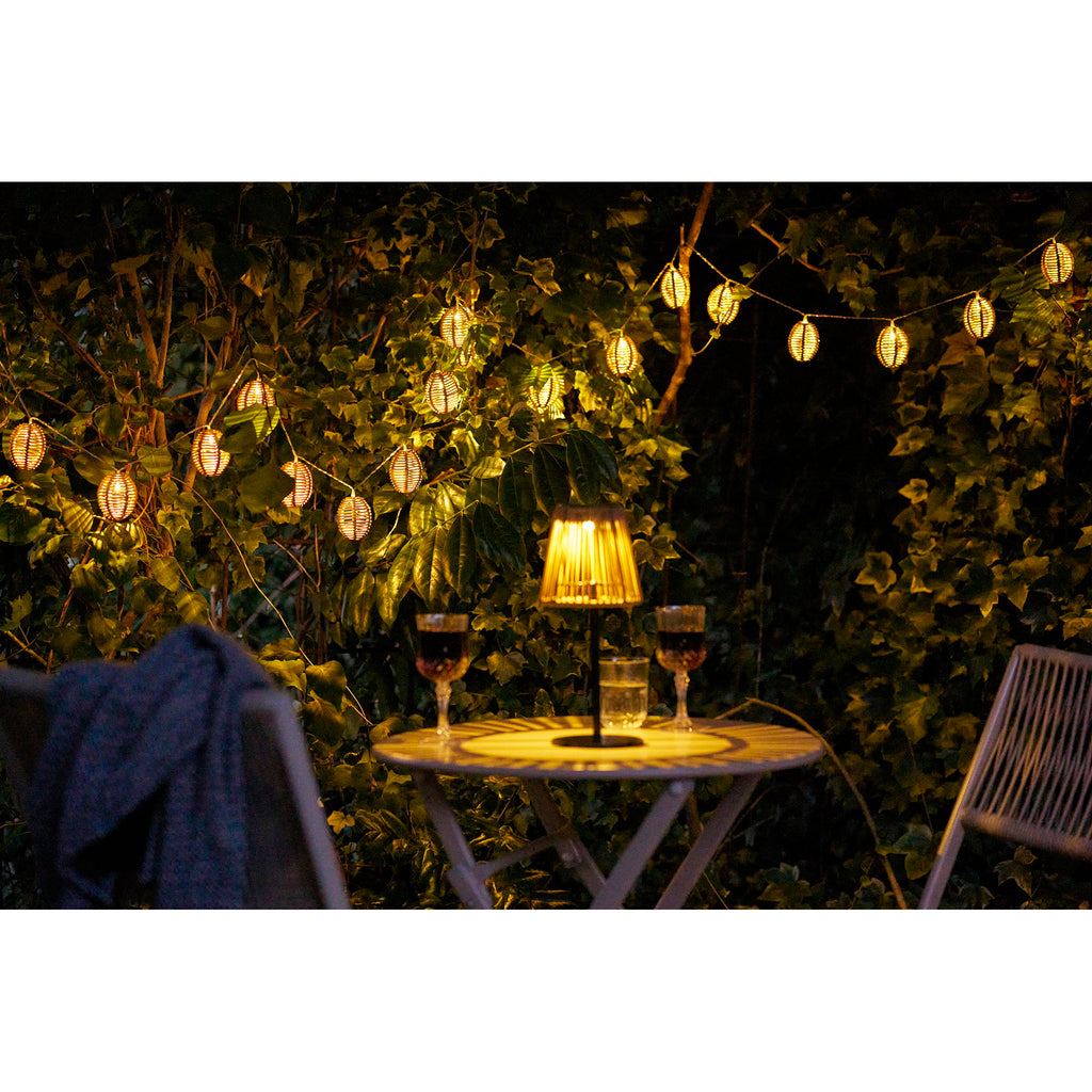Guirlande Carlisle allumée de nuit dans jardin avec lampe table bistrot