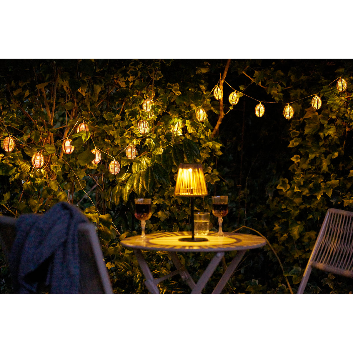 Guirlandes Carlisle allumées dans les arbres derrière une table de bistrot la nuit