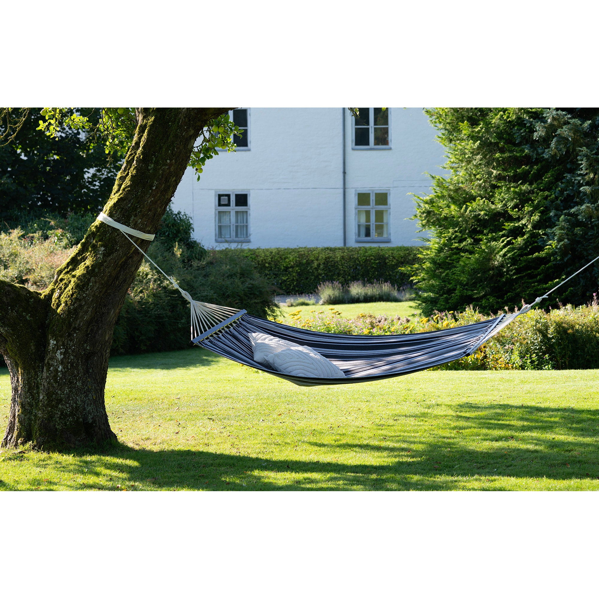 Hamac Lamia rayé noir gris suspendu entre arbres dans jardin avec coussin