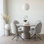 Herbe décorative artificielle beige sable dans un vase blanc près d'une fenêtre à côté d'une table ronde et de chaises bouclées