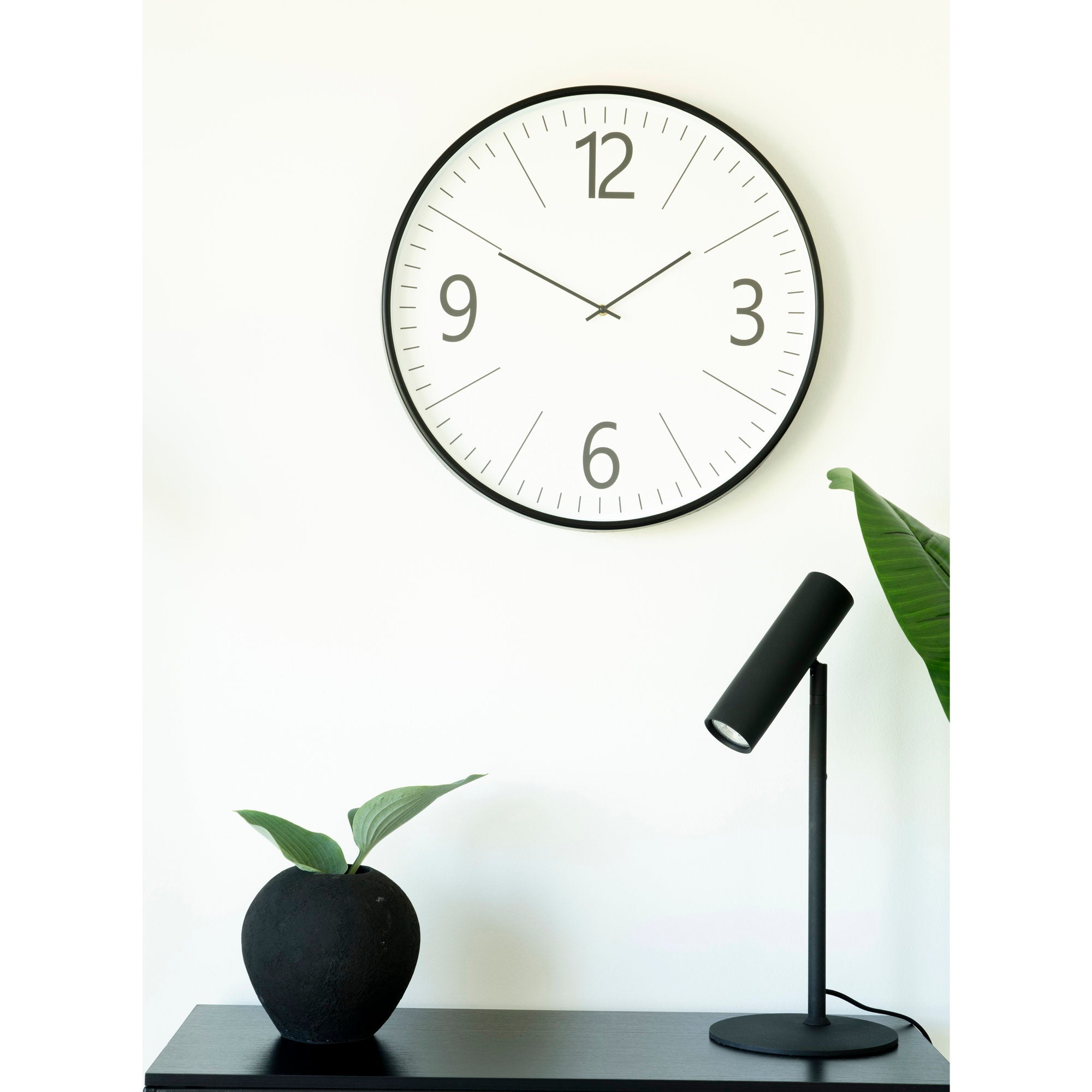 Grande horloge Biel noir blanc en ambiance minimaliste meuble noir lampe spot plante tropicale