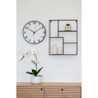 Horloge Greenwich grise au mur au-dessus d'un buffet en bois à côté d'une étagère en métal noir