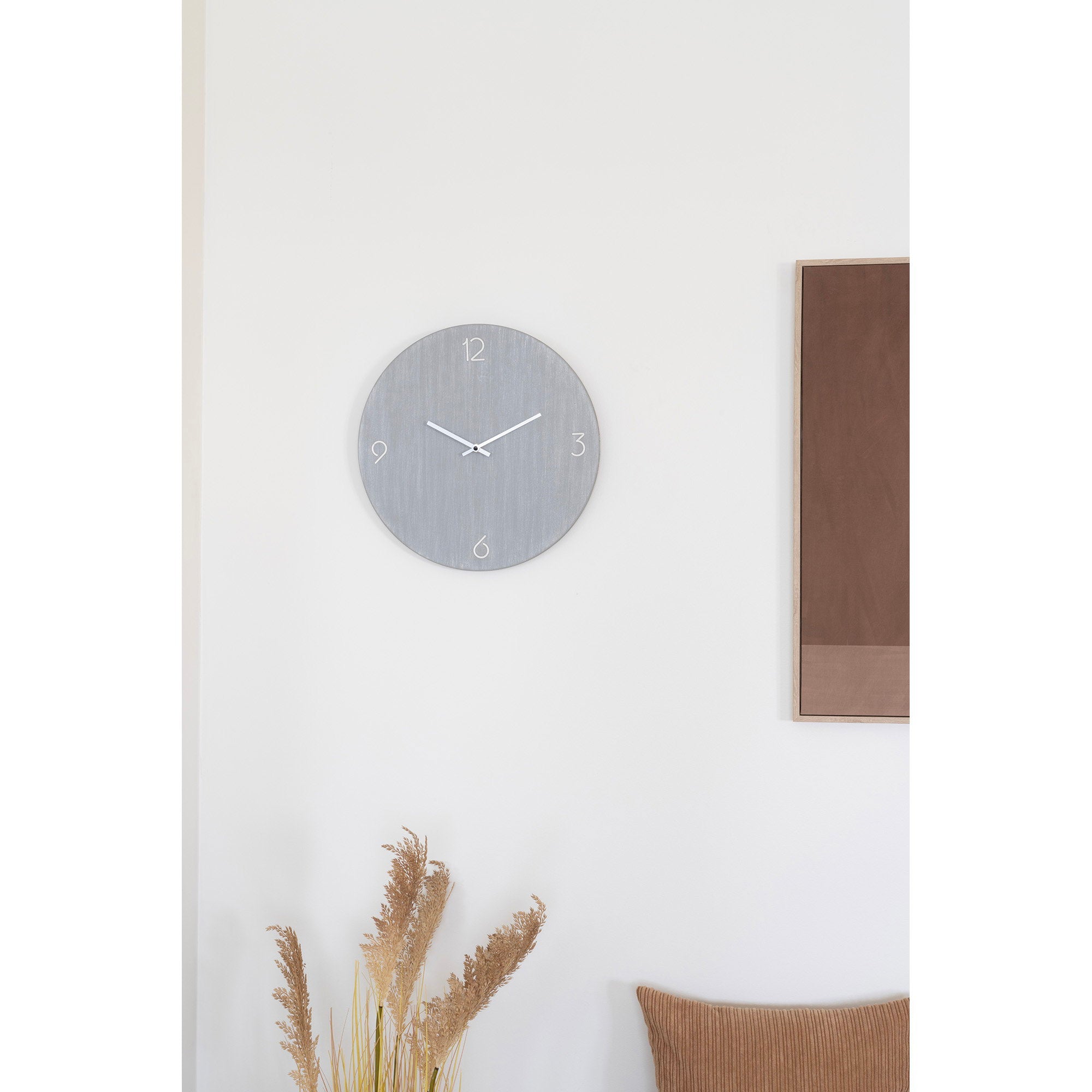 Horloge murale Ravenna gris clair en ambiance salon épuré mur blanc herbes de la pampa