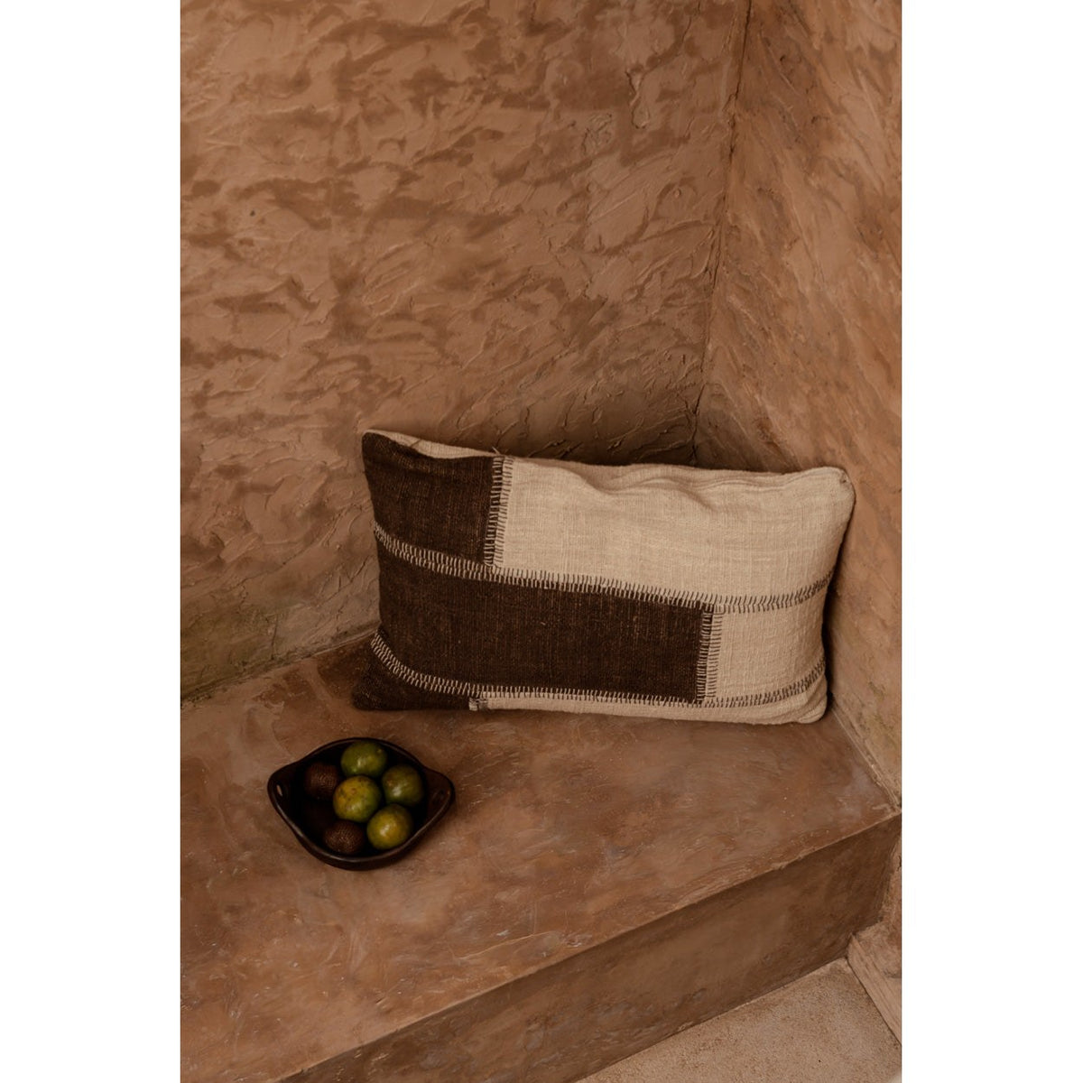 Housse de coussin Cocoa Patchwork sur une banquette en enduit à côté d'une coupe de fruits