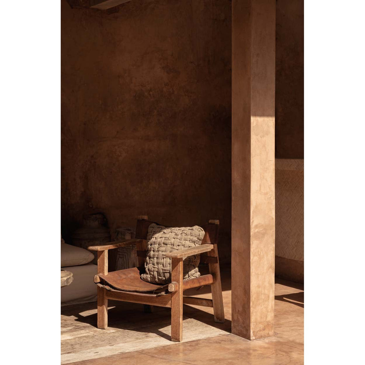 Coussin Crosier sur un fauteuil en bois dans une pièce aux murs enduits près d'un pilier