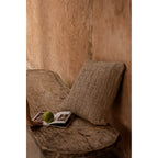 Coussin Damier en lin adossé dans un coin de banc en bois brut avec un livre ouvert