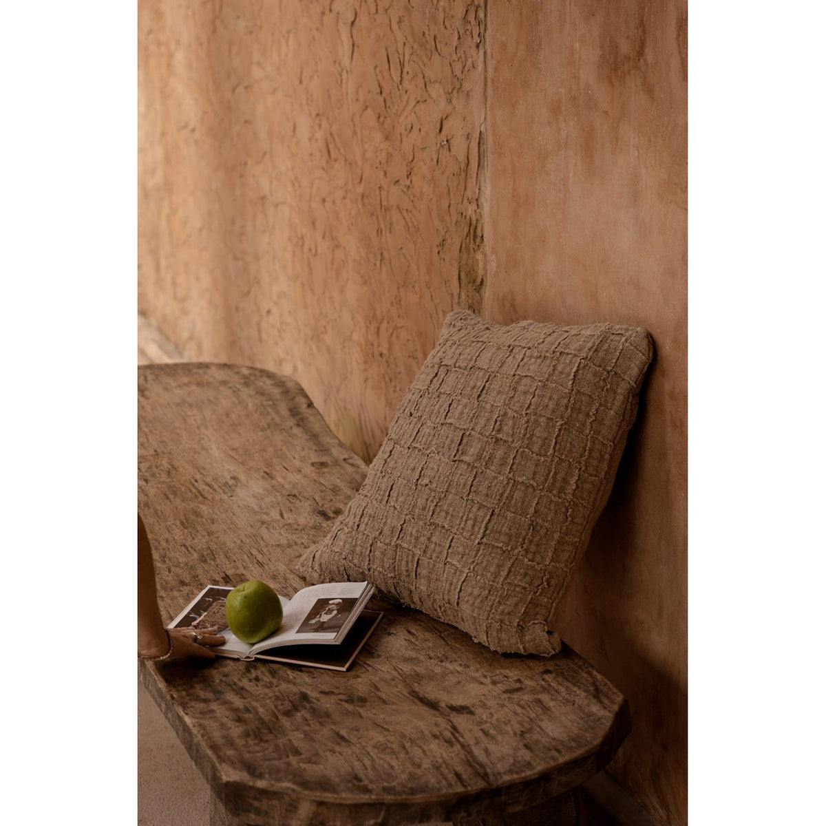 Coussin Damier en lin adossé dans un coin de banc en bois brut avec un livre ouvert