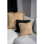 Coussin Flores en raphia au premier plan d'un coussin en raphia à franges et d'un coussin noir sur un canapé gris clair