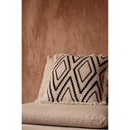 Housse de coussin Sahara Diamond de trois quarts sur une assise écrue devant un mur terracotta