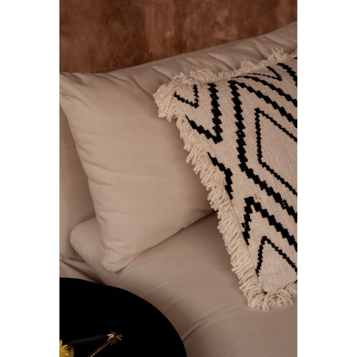 Détail de la frange écrue de la housse de coussin Sahara Diamond posée contre un coussin uni