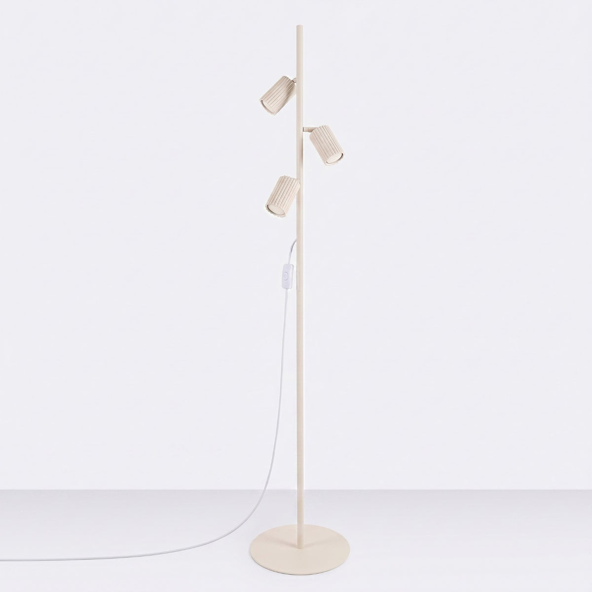 Lampadaire Karbon laque beige à trois spots éteints sur sa base ronde devant un fond uni
