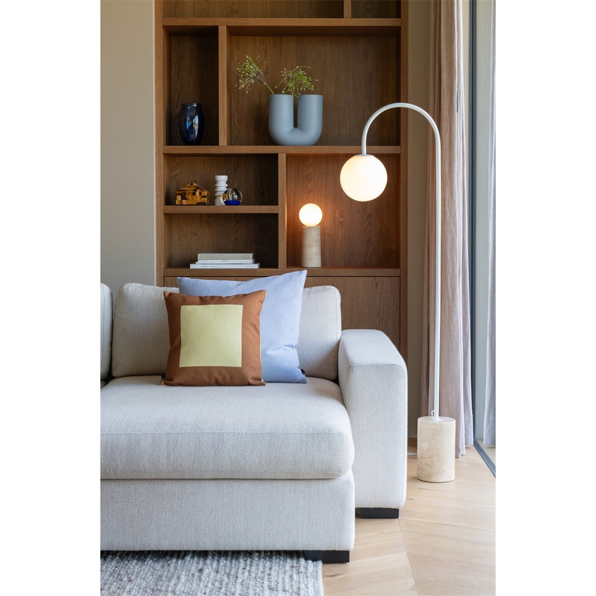 Lampadaire globe Tivoli travertin blanc allumé devant une bibliothèque en bois près d'un canapé avec une lampe à poser en arrière-plan