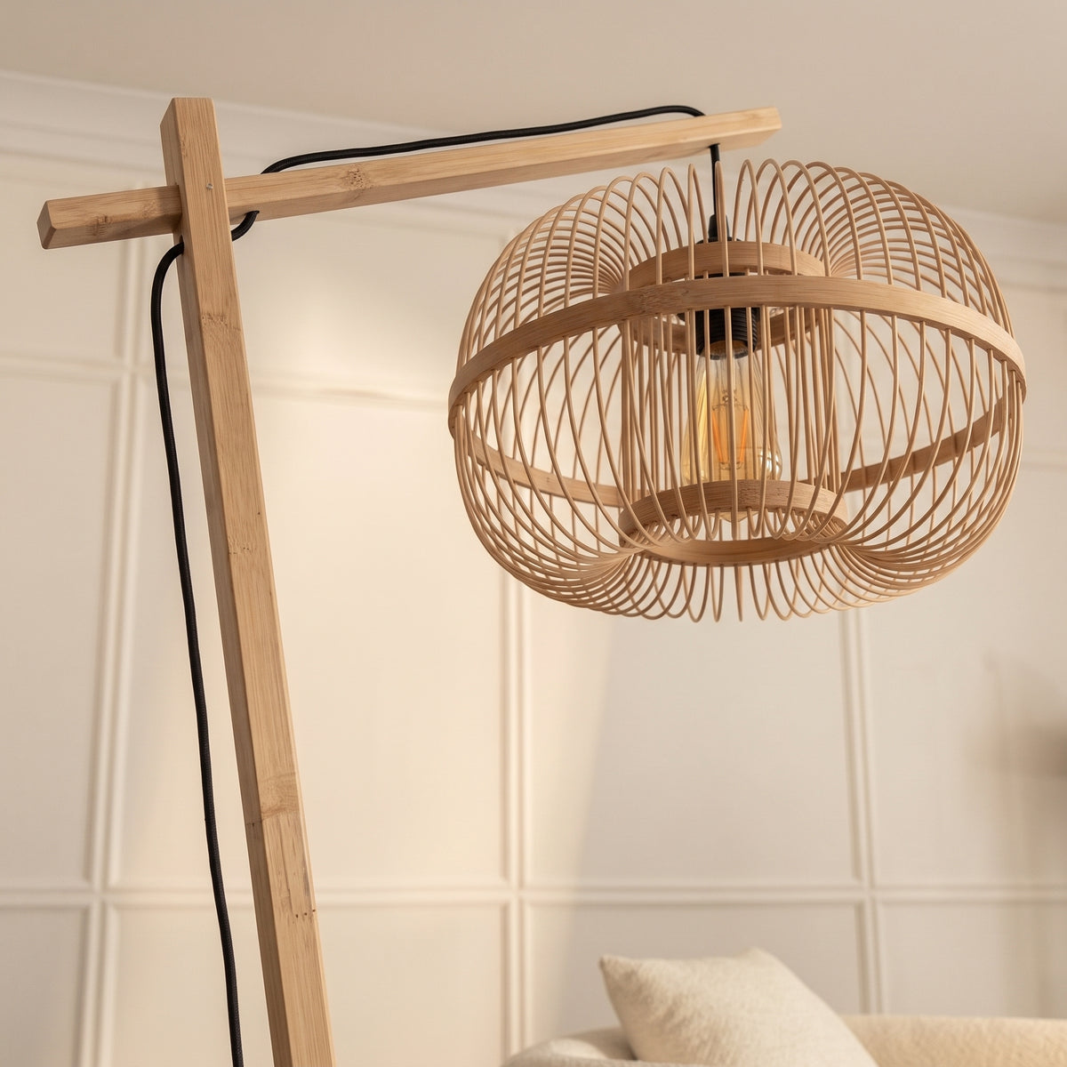 Bras déporté en bambou naturel et abat-jour cage du lampadaire Hokkaido allumé devant un mur à moulures