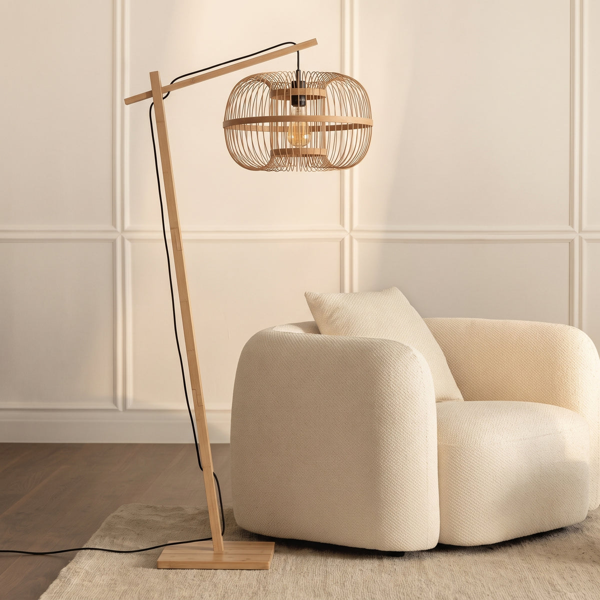 Lampadaire liseuse Hokkaido en bambou naturel allumé à côté d'un fauteuil bouclette écru