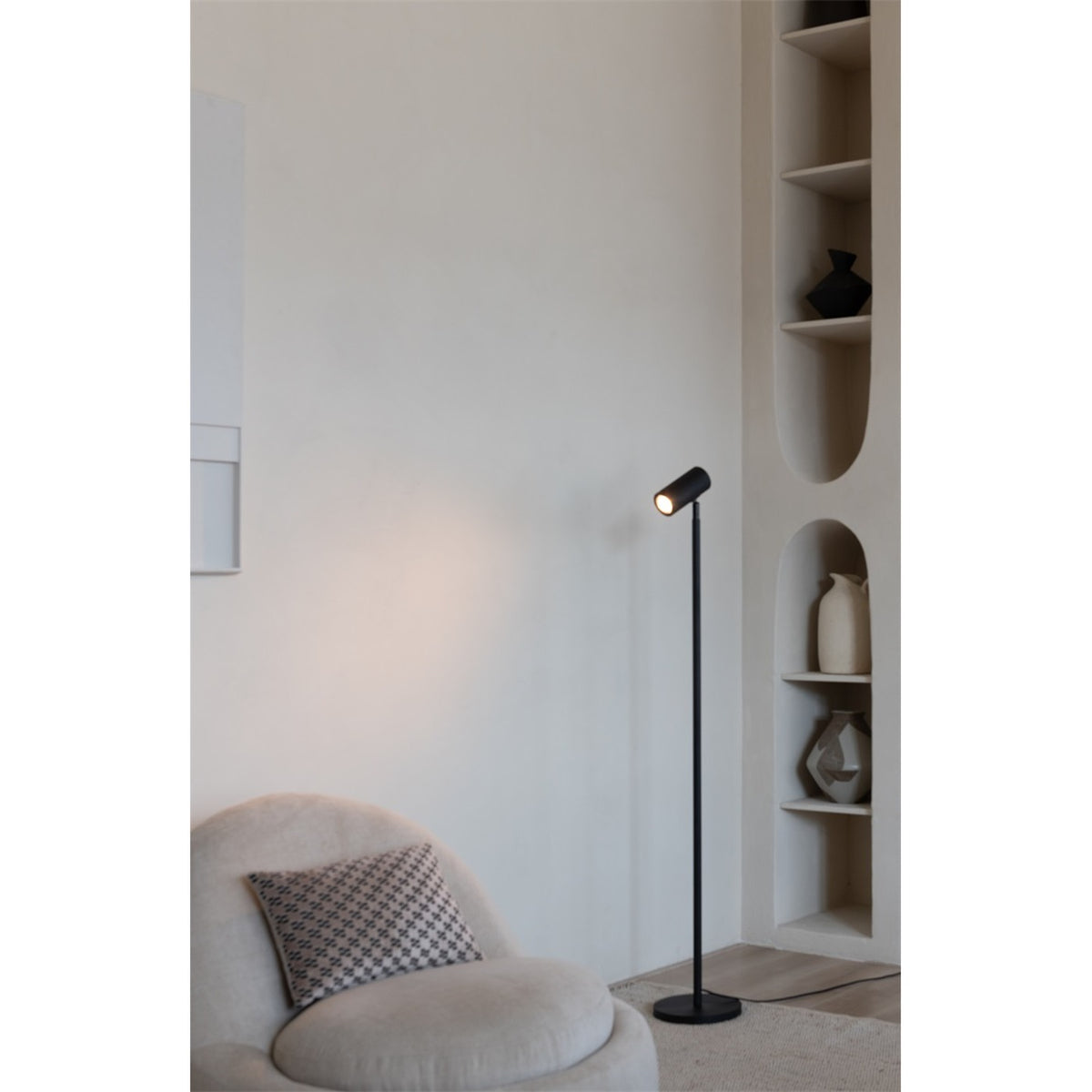 Lampadaire liseuse Java bambou noir allumé près d'un fauteuil rond et de niches à vases