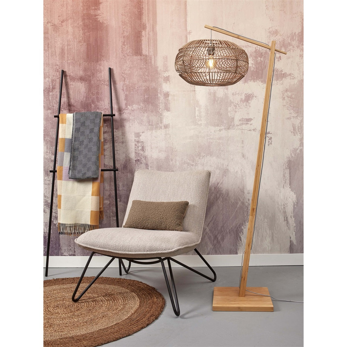 Lampadaire liseuse Madeira bambou naturel à côté d'un fauteuil bouclé et d'un tapis rond en jute devant un mur rose