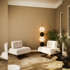 Lampadaire Tama allumé entre deux fauteuils blancs à poils longs devant un mur sable