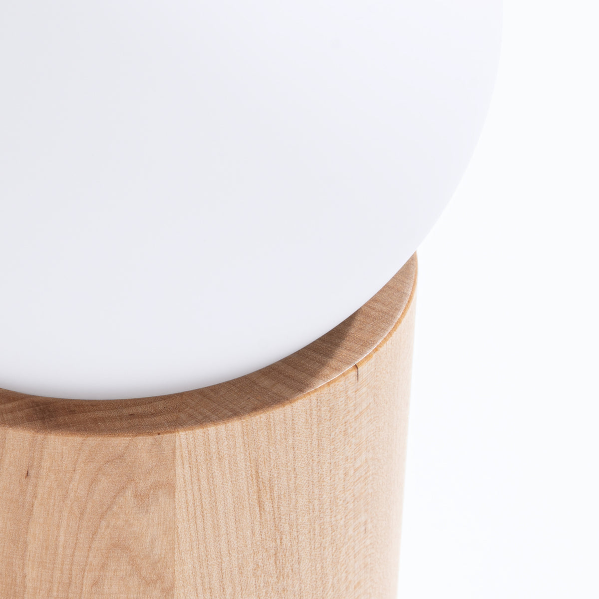 Détail de la boule de verre opale nichée dans le socle en bois clair de la lampe Boomo