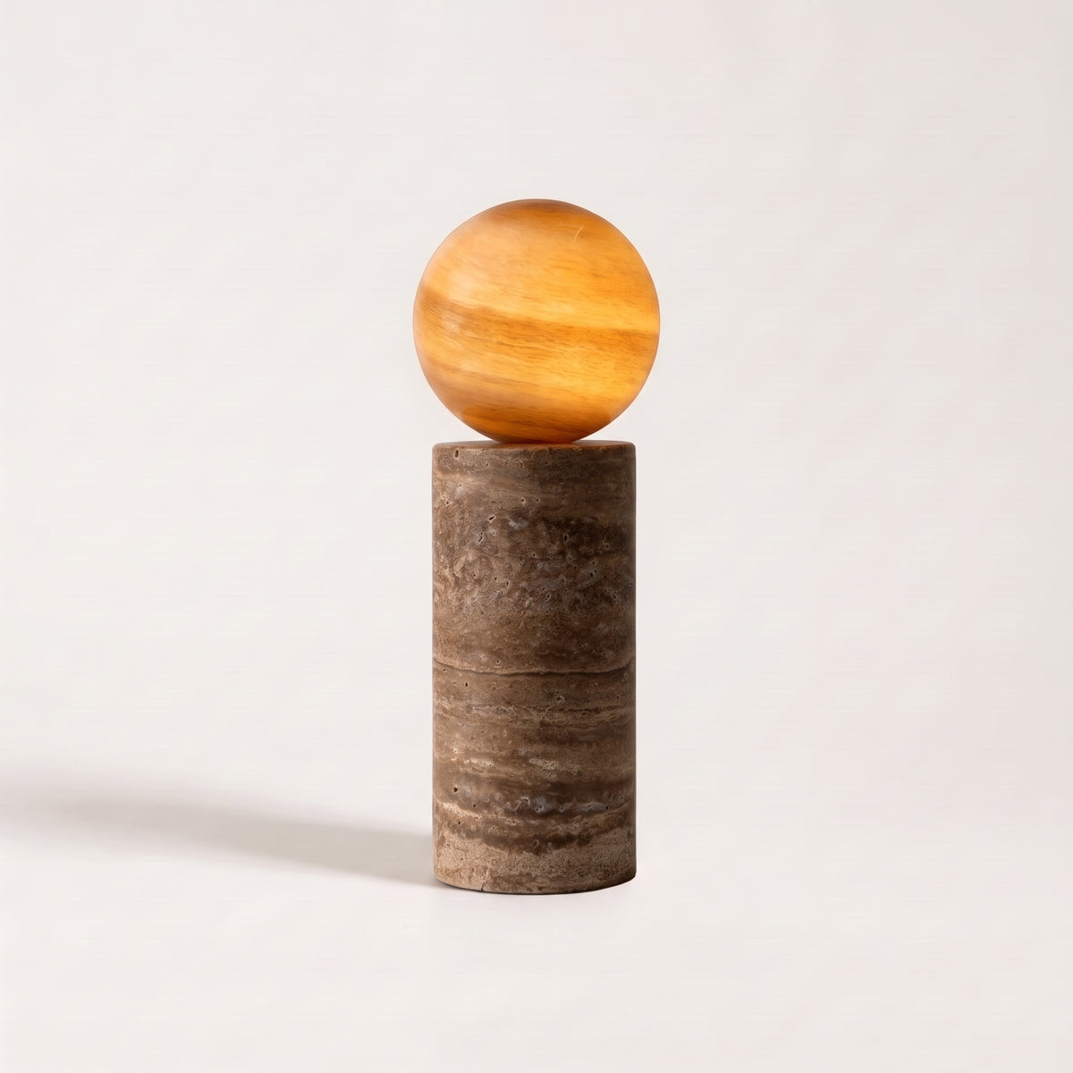 Lampe à poser Tivoli, socle en travertin sable veiné de brun et globe en verre ambré allumé, sur fond clair
