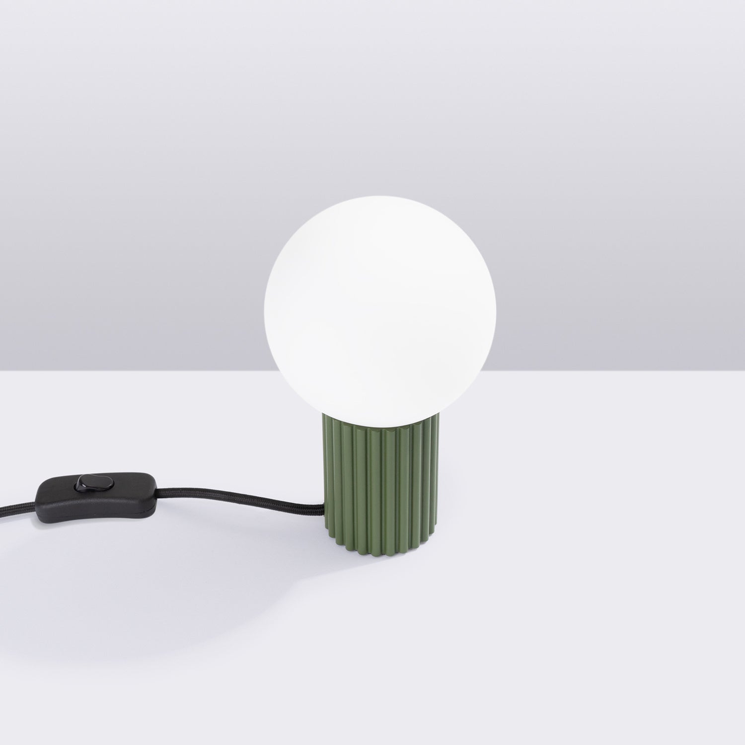 Lampe à poser Halo boule opale vert olive posée sur une table de chevet