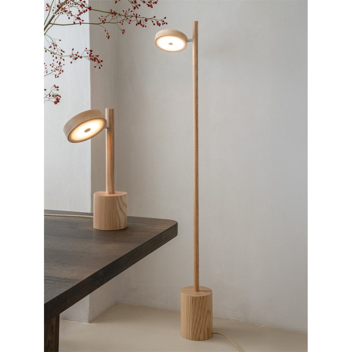 Lampe Okinawa frêne naturel allumée sur une table en bois sombre à côté du lampadaire de la même ligne