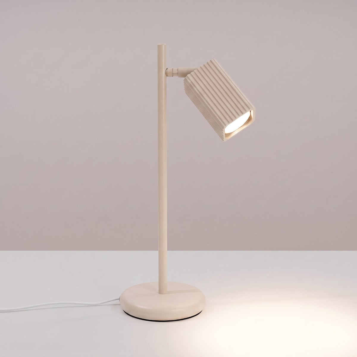 Lampe à poser Rayo laque beige allumée avec son faisceau dirigé sur la table