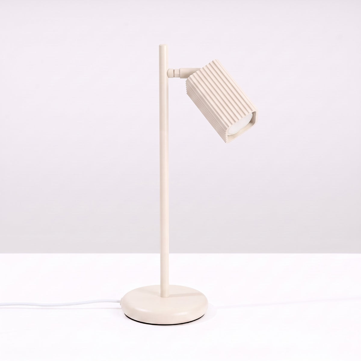 Lampe à poser Rayo laque beige posée sur une table devant un mur clair