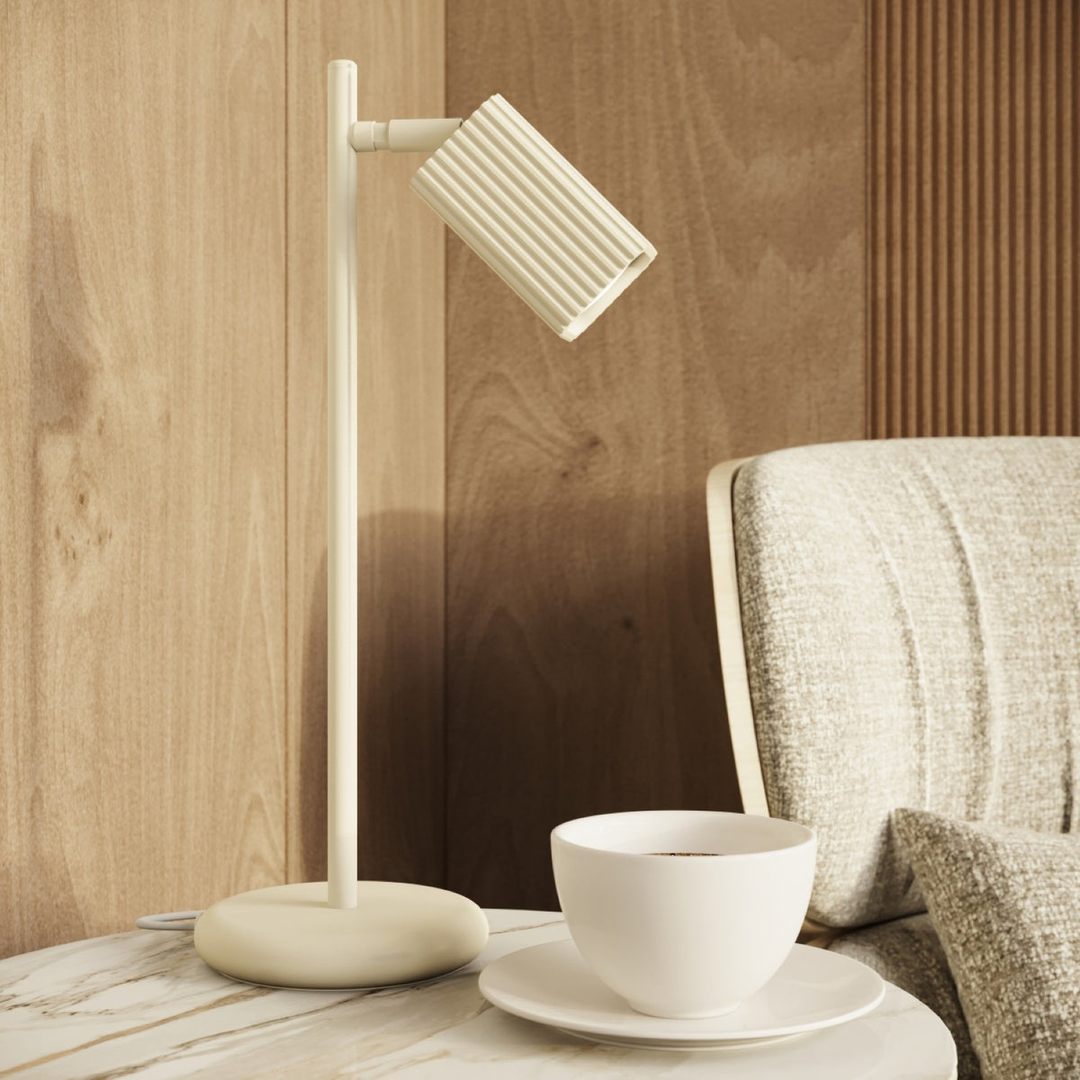 Lampe à poser Rayo laque beige sur une table d'appoint ronde près d'un fauteuil