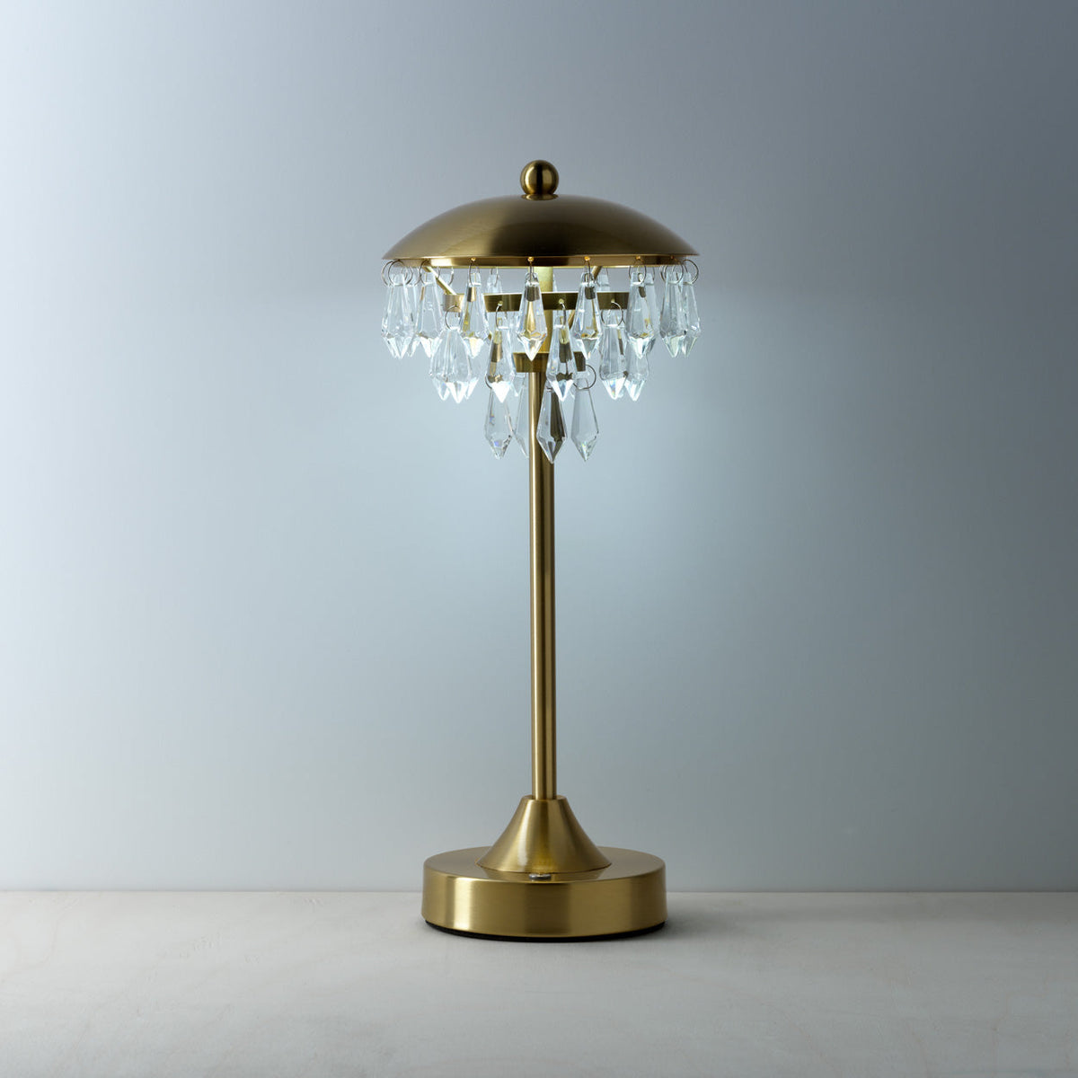 Lampe Chandelette allumée devant un fond gris avec les pampilles qui accrochent la clarté