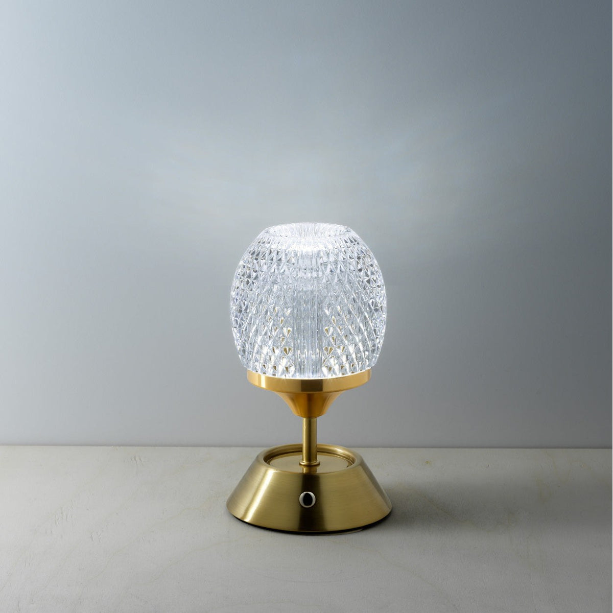 Lampe Glow Sinatra allumée en lumière blanche devant un mur gris