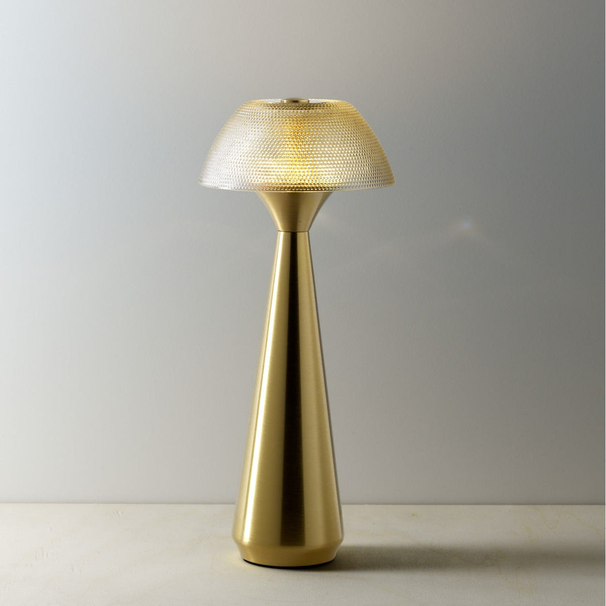 Lampe Mushlampio allumée en lumière chaude sur une table claire devant un mur gris