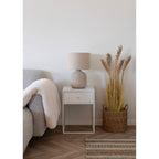 Lampe Bilby céramique blanc cassé sur une table de chevet blanche avec pampas dans une chambre