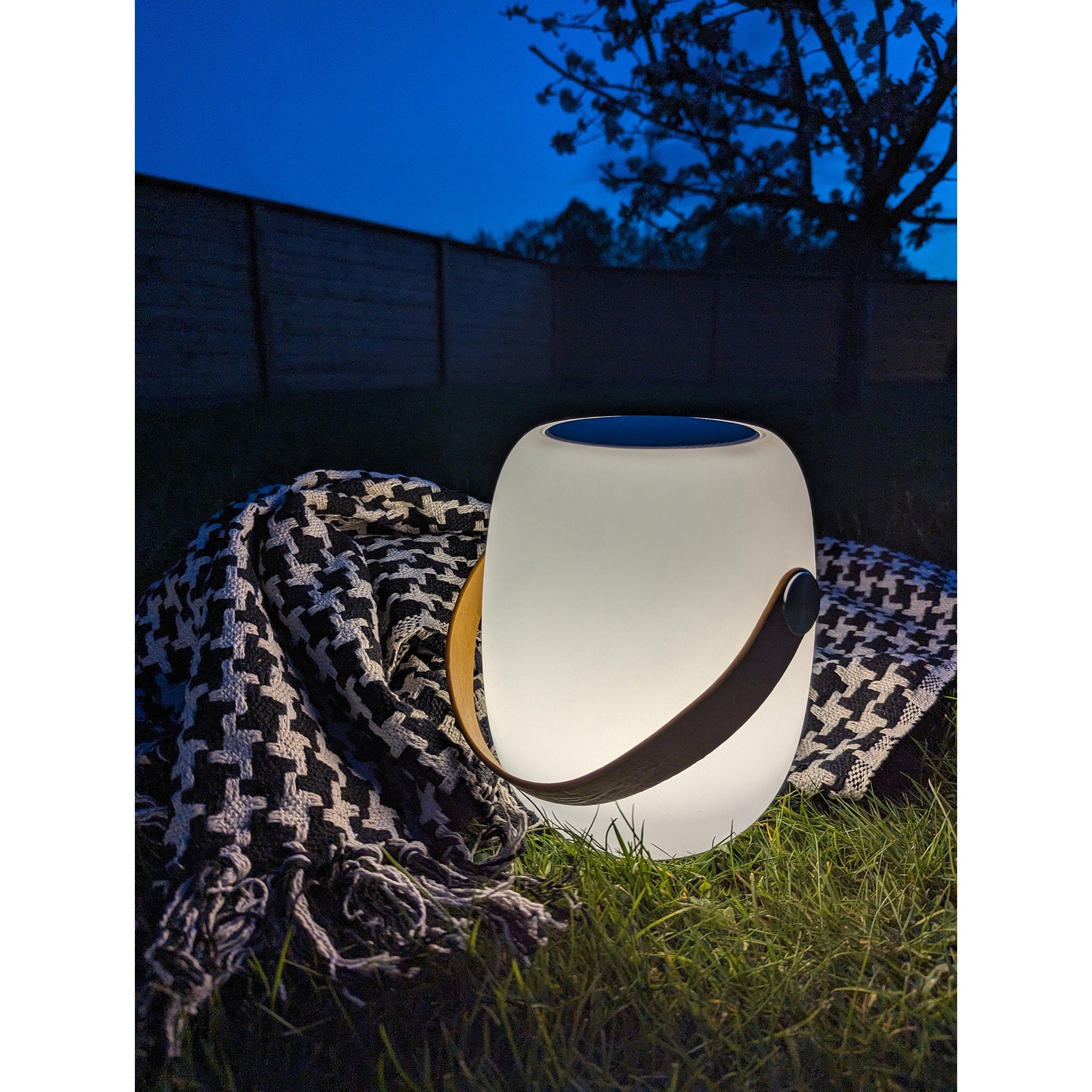Lampe Cardiff blanche allumée posée dans herbe jardin nuit ambiance chaleureuse plaid