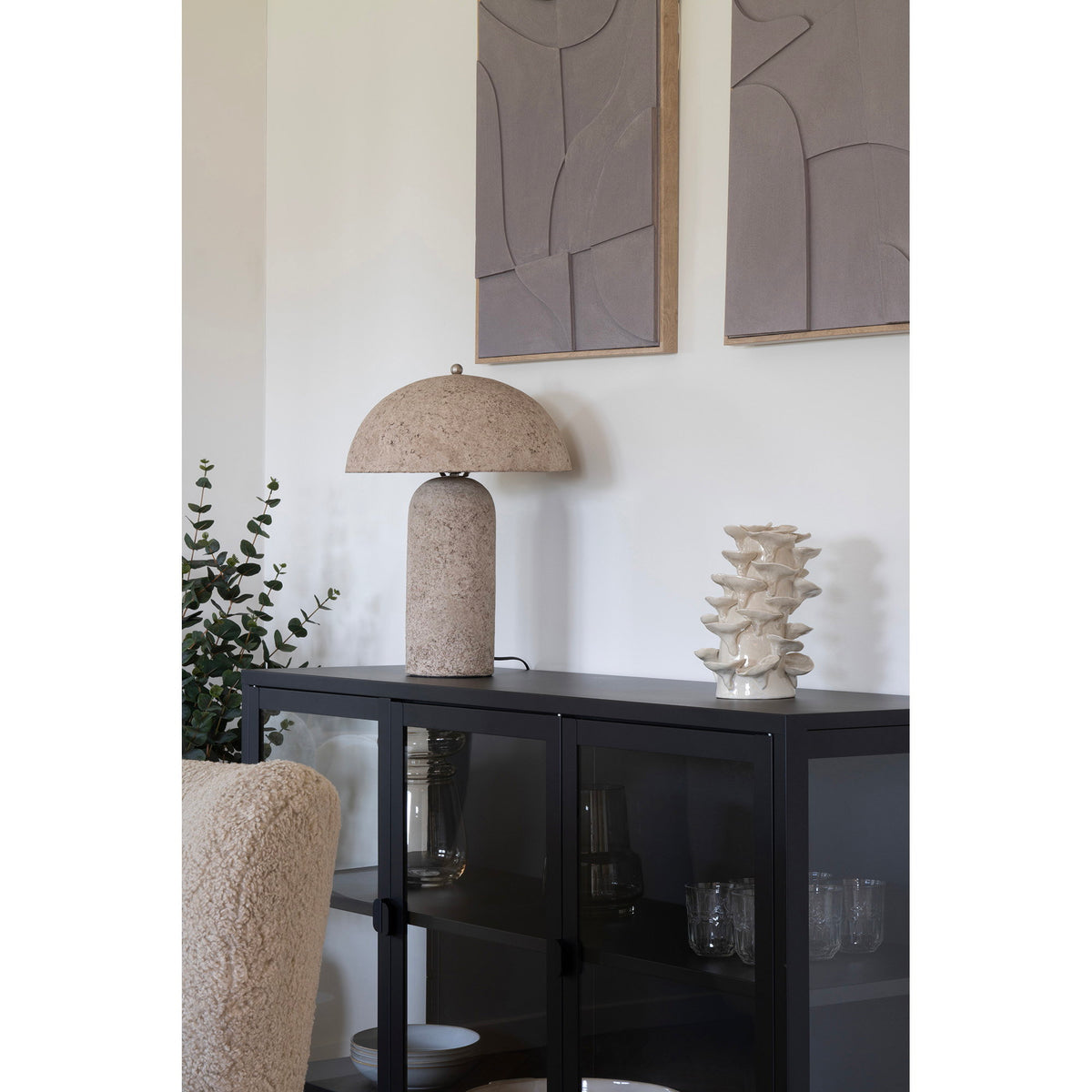 Lampe Astley posée sur un buffet vitré noir sous deux tableaux en relief