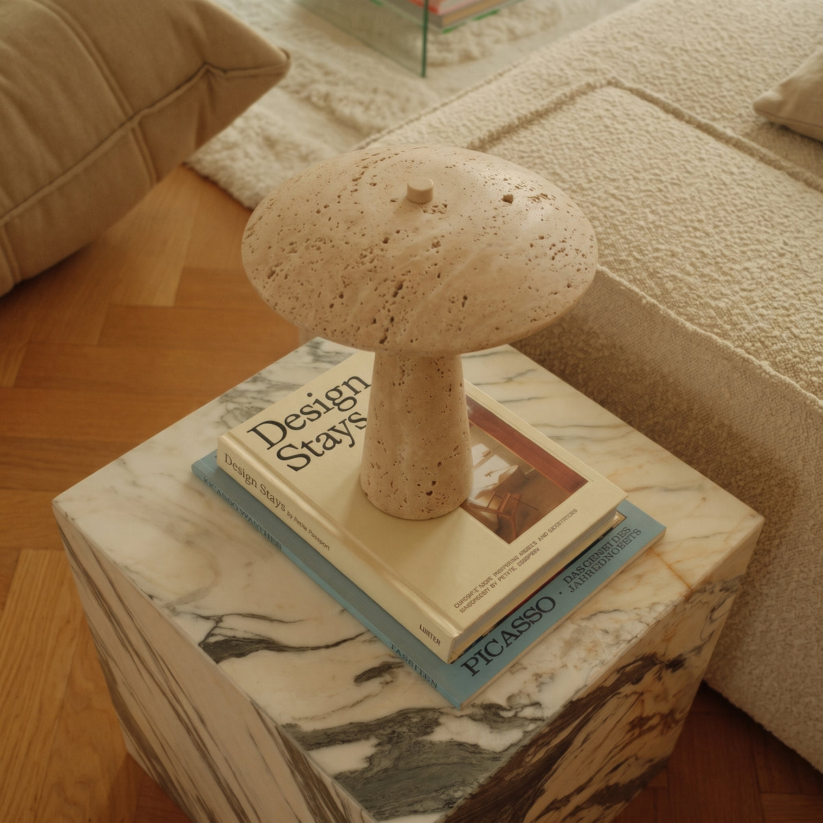 Lampe de table champignon Consett posée sur deux livres sur un cube en marbre veiné, près d'un canapé en bouclé crème