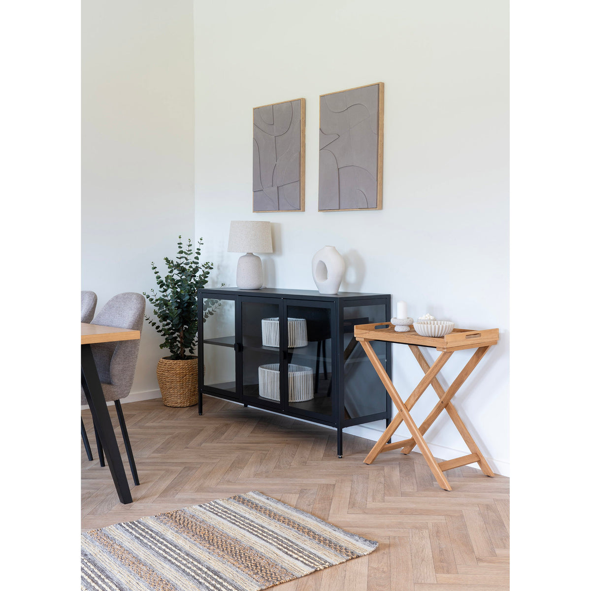 Lampe Croft sur un buffet noir vitré à côté d'un vase blanc et d'une table plateau en bois