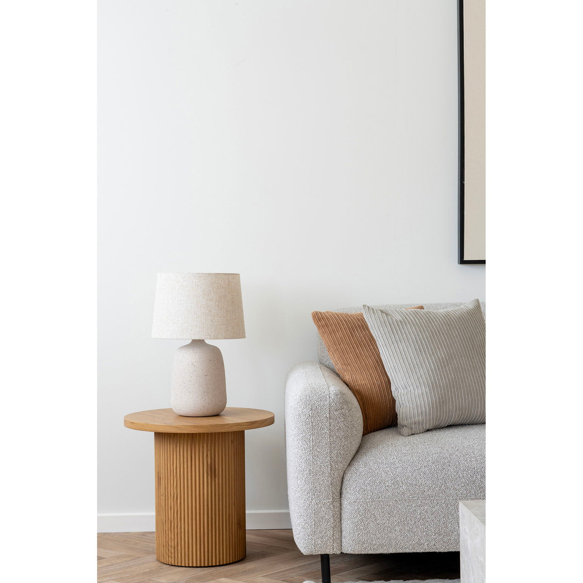 Lampe Croft sur une table d'appoint ronde en bois cannelé à côté d'un canapé gris