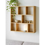 Lampe Ashford allumée dans une case d'étagère murale en bois clair au-dessus d'un canapé gris
