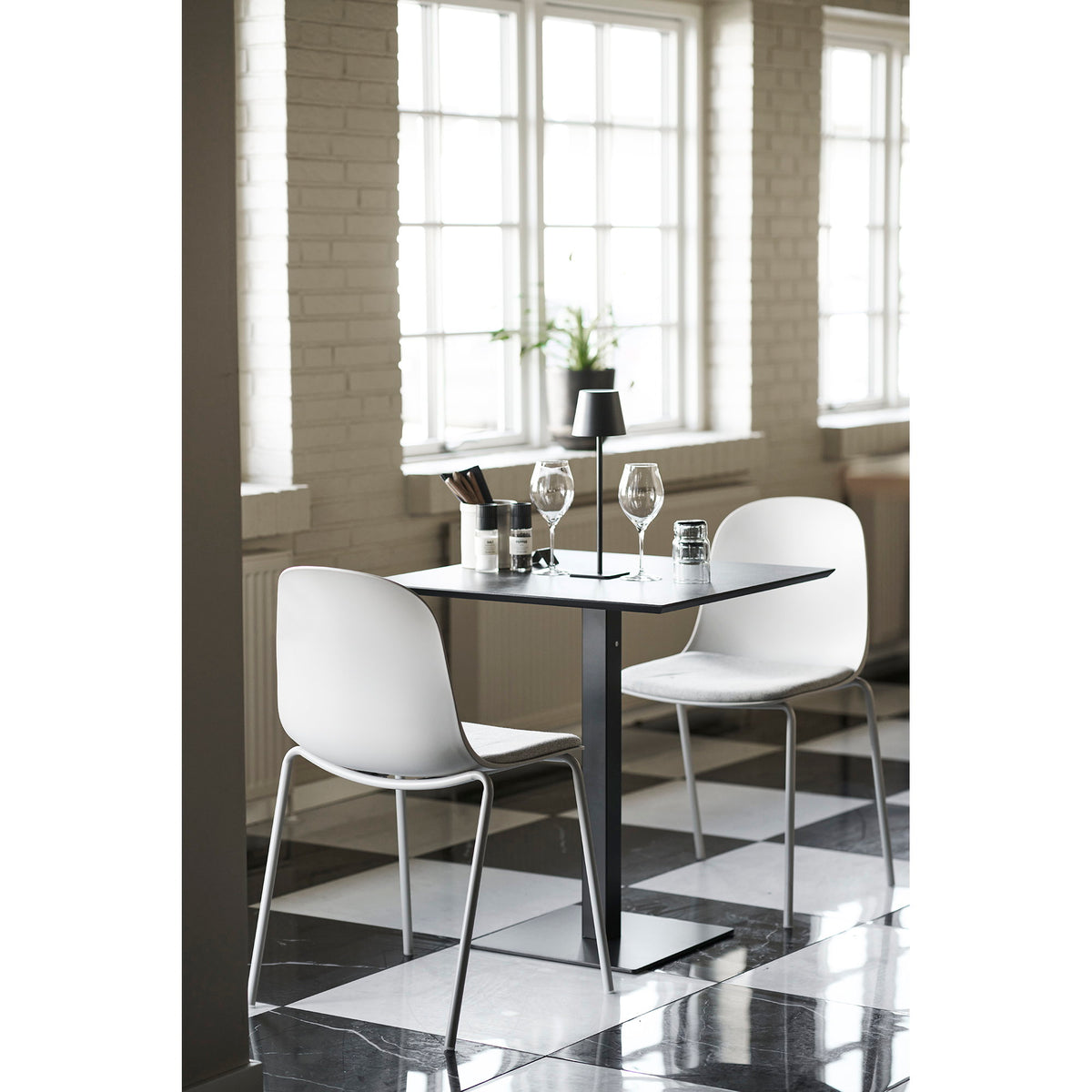 Lampe Bradford noire sur une table carrée noire entourée de deux chaises blanches