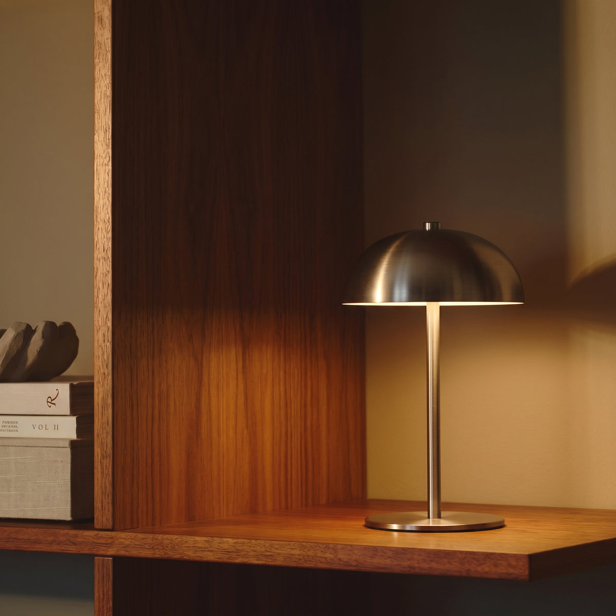 Lampe de table sans fil Fenwick allumée sur une étagère en bois foncé, près de livres empilés, lumière chaude