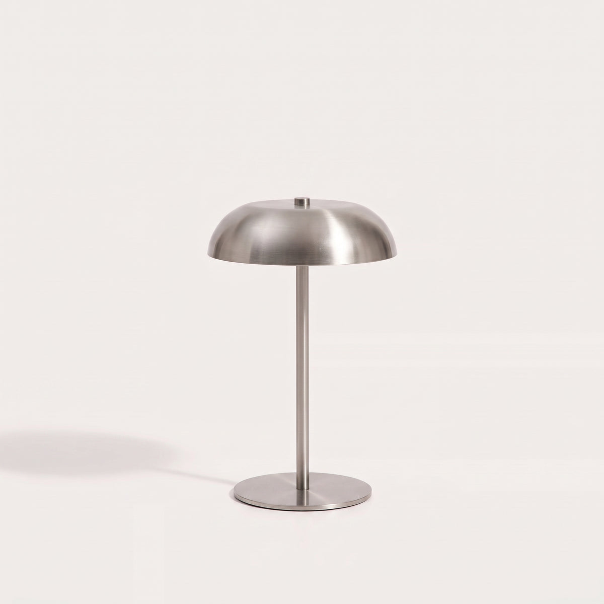 Lampe de table sans fil Fenwick éteinte sur fond clair, dôme, tige fine et socle rond en métal brossé argenté