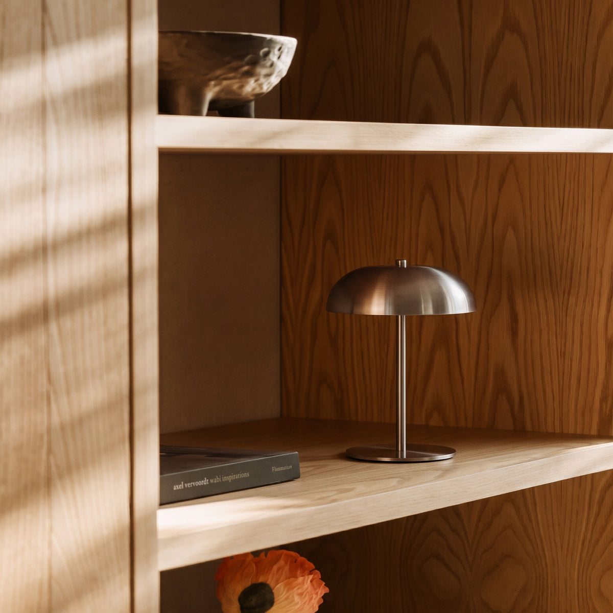 Lampe de table sans fil Fenwick sur l'étagère d'une bibliothèque en bois clair, près d'un livre et d'un bol en céramique