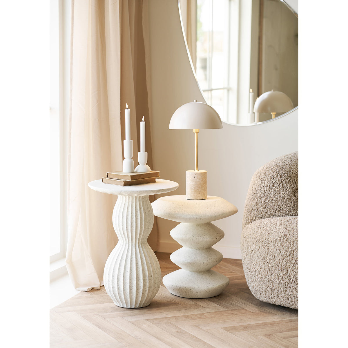 Lampe Sheffield sur une table d'appoint sculpturale blanche près d'un miroir rond et de deux bougeoirs blancs