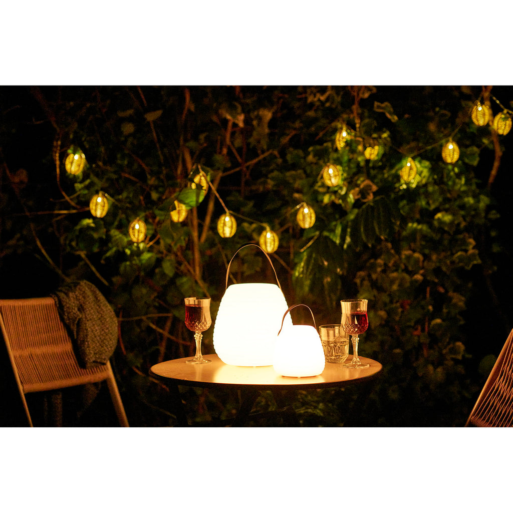 Grande lampe Derry allumée sur table de jardin la nuit, ambiance romantique lumière chaude
