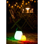 Deux lampes lanternes Derry LED RGB éclairant un jardin la nuit en couleurs verte et jaune
