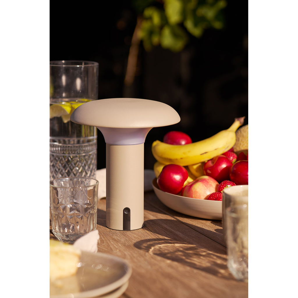 Lampe portable Ramsey beige sur table de repas extérieure entourée de fruits et verres